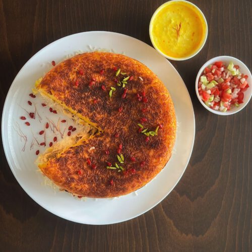 Ganzes Safran-Hähnchen-Tahchin mit goldener Kruste, angeschnitten und mit Berberitzen, Safranfäden und Pistazien garniert, serviert mit Safransauce und Shirazi-Salat